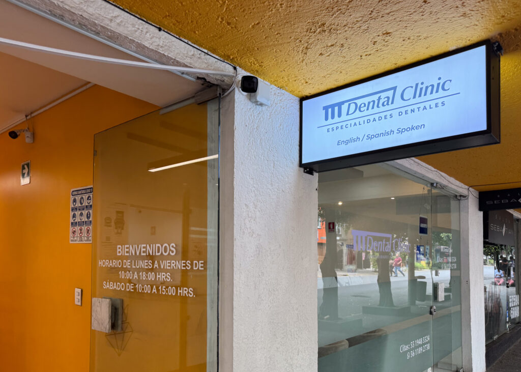 A sign hanging above a door that says "M Dental Clinic, Especialidades Dentales, English/Spanish Spoken"