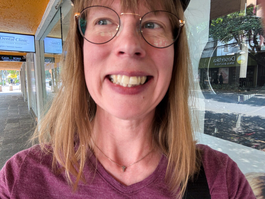 Chrissy standing outside the dental clinic, smiling wide to show her clean teeth.