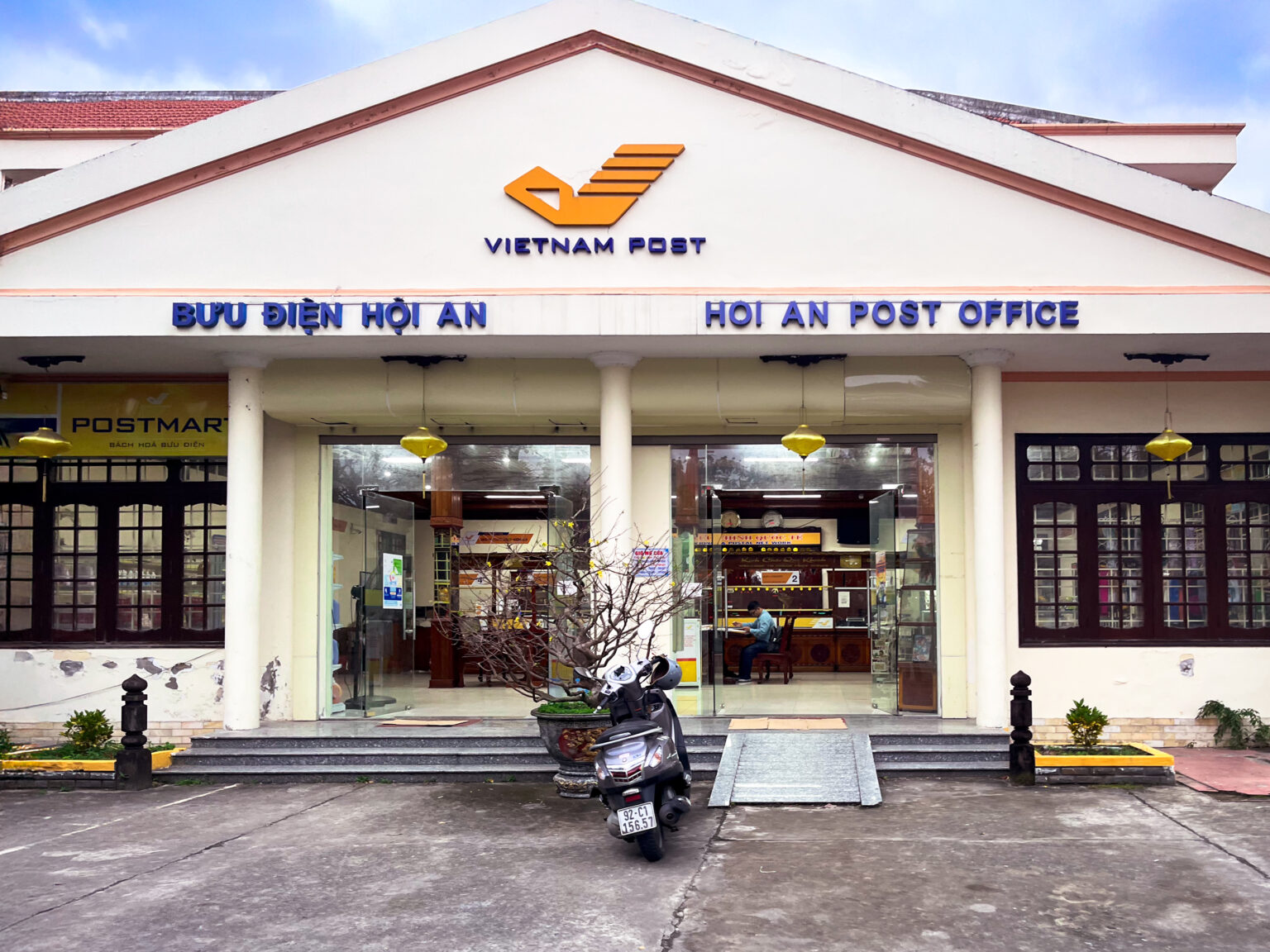 Exterior photograph of the post office in Hoi An Vietnam with a motorcycle parked in front of the entrance.